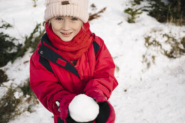 Nahaufnahme eines niedlichen Mädchens, das einen Schneeball zeigt, während es auf einem schneebedeckten Grundstück steht - JVSF00014