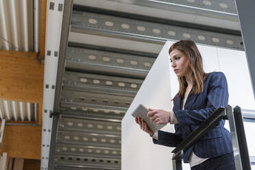 Businesswoman holding digital tablet looking away while standing by railing in factory - DIGF12703