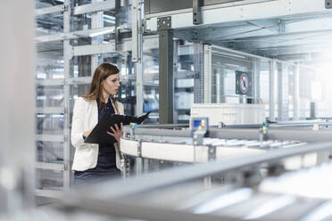 Female manager holding file while examining production line in factory - DIGF12724