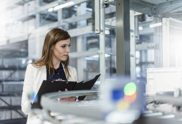 Female manager holding file while examining production line in factory - DIGF12725