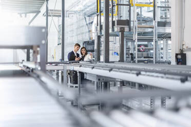 Professionals discussing while examining production line in factory - DIGF12728