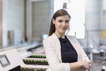 Confident businesswoman with arms crossed standing in factory - DIGF12730