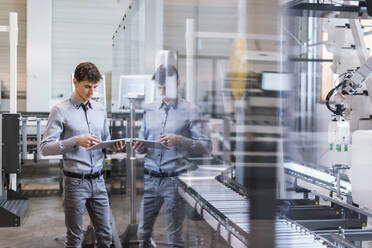 Male professional using digital tablet while standing by production line in factory - DIGF12738