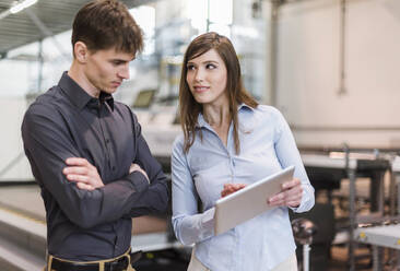 Geschäftsfrau zeigt einem männlichen Kollegen ein digitales Tablet, während sie in einer Fabrik steht - DIGF12743
