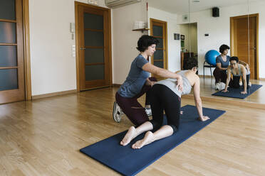 Physiotherapist assisting female patient in exercising on mat at health club - XLGF00220