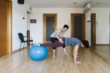 Physiotherapeutin hilft Patientin beim Balancieren auf dem Fitnessball im Fitnessstudio - XLGF00221