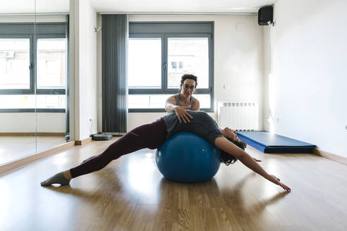 Physiotherapist assisting patient in lying on fitness ball at health club - XLGF00222