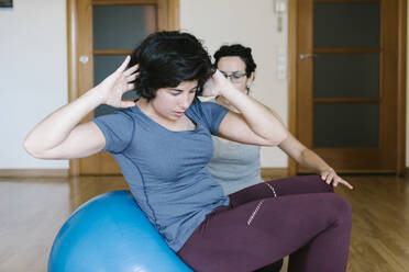Physiotherapeutin unterstützt Patientin bei Übungen mit dem Fitnessball im Fitnessstudio - XLGF00223