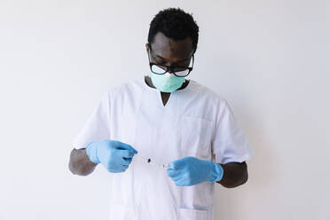 Afro-Arzt, der eine Spritze und ein Fläschchen hält, während er vor einem weißen Hintergrund steht - JCMF00852