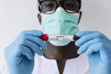 Nahaufnahme eines afroamerikanischen Arztes, der eine Blutprobe des Coronavirus hält, vor weißem Hintergrund - JCMF00854