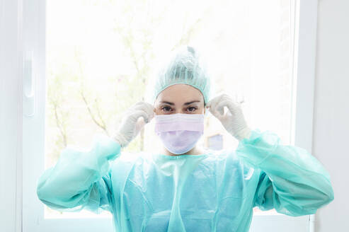 Nahaufnahme einer Krankenschwester mit chirurgischer Maske vor einem Fenster im Krankenhaus - JCMF00864