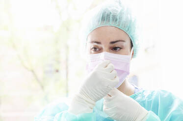 Close-up of female nurse wearing surgical mask against window in hospital - JCMF00865