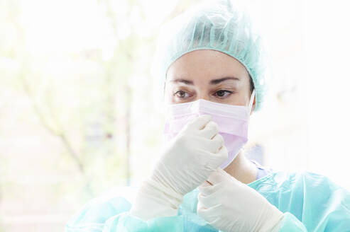 Nahaufnahme einer Krankenschwester mit chirurgischer Maske vor einem Fenster im Krankenhaus - JCMF00865