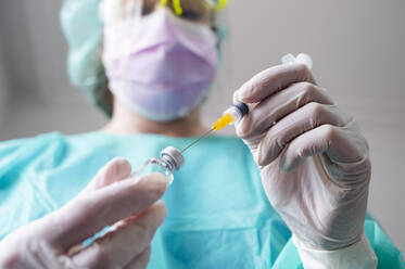 Close-up of nurse holding coronavirus vaccine and syringe in clinic - JCMF00869