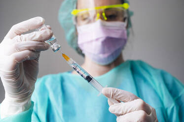 Close-up of female nurse holding coronavirus vaccine and syringe in clinic - JCMF00870