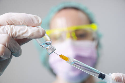 Nahaufnahme der Hände eines Zahnarztes, der den Coronavirus-Impfstoff und die Spritze in der Klinik hält - JCMF00871