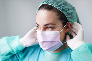 Close-up of female nurse wearing surgical mask looking away in clinic - JCMF00875