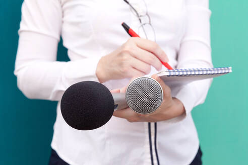 Nahaufnahme einer Frau mit Mikrofon und Notizblock vor farbigem Hintergrund - EYF06759