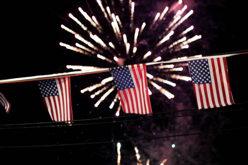 Low Angle View of American Flags Hanging Against Firework Display in der Nacht - EYF06798