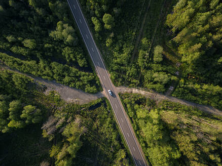 Russland, Leningrad Oblast, Tichwin, Luftaufnahme eines Autos auf einer asphaltierten Straße, die durch einen großen grünen Wald führt - KNTF04698