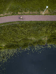 Russland, Tichwin, Luftaufnahme einer Radfahrerin, die auf einem Fußweg am Seeufer im Park eine Pause einlegt - KNTF04705