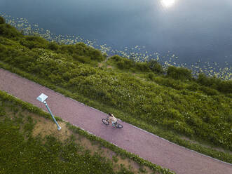 Russland, Tichwin, Luftaufnahme einer Radfahrerin auf einem Fußweg am Seeufer im Park - KNTF04707