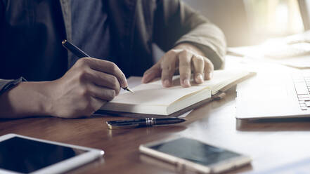 Midsection Of Businessman Writing In Book On Table - EYF06898