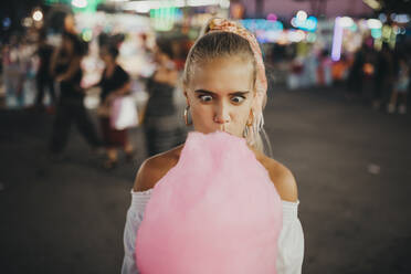 Close-up of woman making face while eating cotton candy at amusement park - MIMFF00069