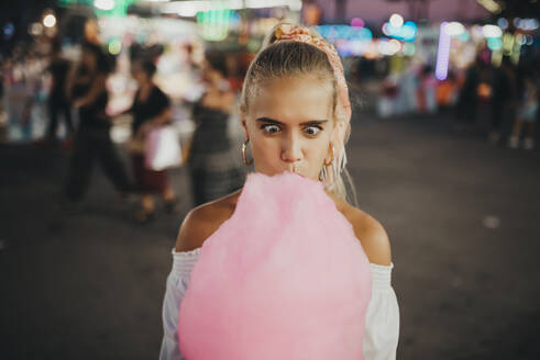 Close-up of woman making face while eating cotton candy at amusement park - MIMFF00069