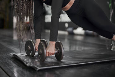 Nahaufnahme einer Sportlerin, die Hanteln hält, während sie auf einer Matte im Fitnessstudio trainiert - VEGF02350