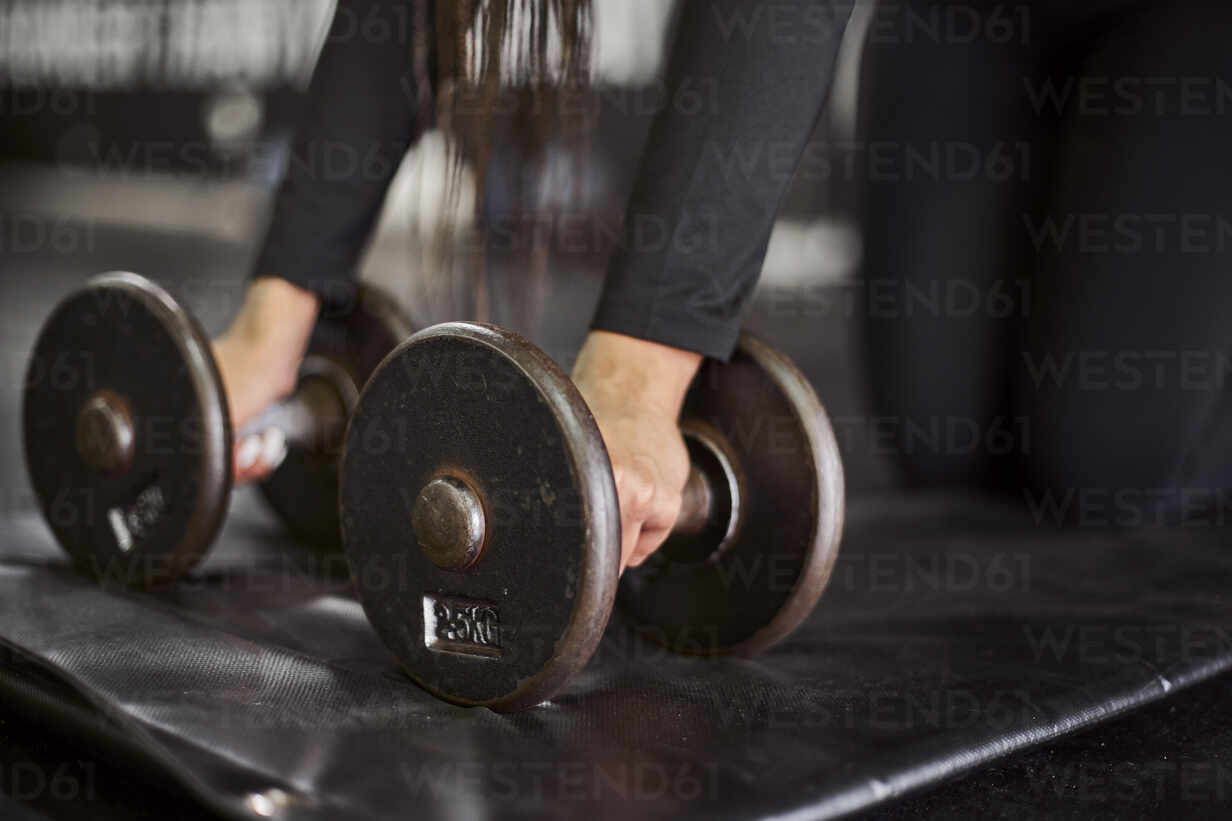Close-up of young woman holding dumbbells on mat in gym stock photo