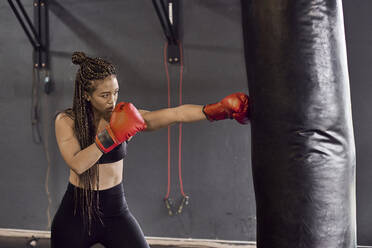 Female boxer wearing red gloves practicing boxing drill on punching bag in gym - VEGF02363