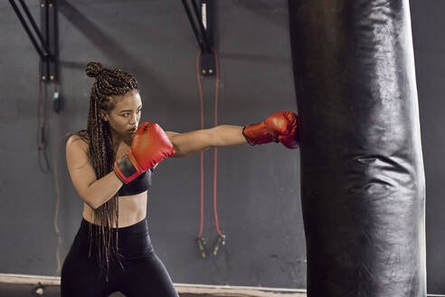 Weiblicher Boxer mit roten Handschuhen übt in einer Turnhalle an einem Boxsack - VEGF02363