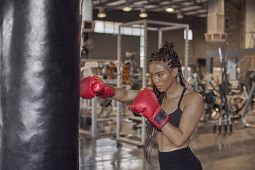 Young woman wearing red gloves practicing boxing drill on punching bag in gym - VEGF02365
