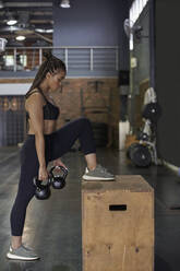 Weibliche Athletin hebt Kettlebells im Stehen im Fitnessstudio - VEGF02380