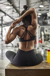 Female athlete stretching hands while sitting on table in gym - VEGF02387