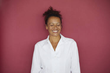 Porträt einer lächelnden Geschäftsfrau mit geschlossenen Augen vor rotem Hintergrund - RBF07736