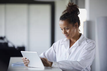 Porträt einer lächelnden Geschäftsfrau, die in einem modernen Büro ein digitales Tablet benutzt - RBF07739