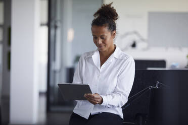 Porträt einer lächelnden Geschäftsfrau, die in einem modernen Büro ein digitales Tablet benutzt - RBF07749