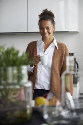 Porträt einer lächelnden Geschäftsfrau, die mit einer Tasse Kaffee in der Küche steht - RBF07756