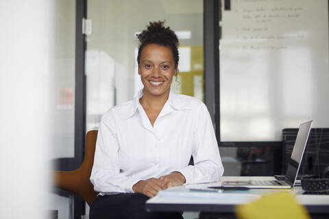 Porträt einer lächelnden Geschäftsfrau, die am Schreibtisch im Büro sitzt, lizenzfreies Stockfoto