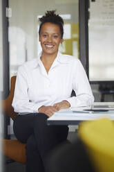 Porträt einer lächelnden Geschäftsfrau, die am Schreibtisch im Büro sitzt - RBF07766
