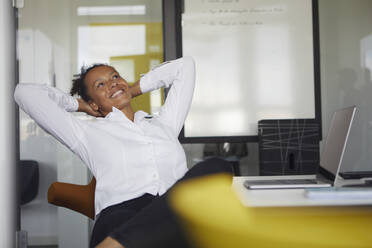 Porträt einer glücklichen Geschäftsfrau, die sich am Schreibtisch im Büro entspannt - RBF07768