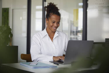 Portrait of smiling businesswoman working on laptop in office - RBF07769