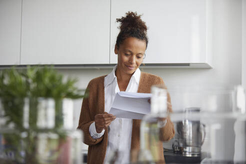 Portrait of smiling businesswoman standing in kitchen looking at contract - RBF07772