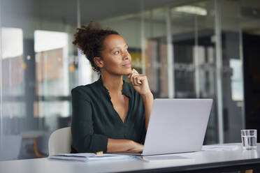Porträt einer nachdenklichen Geschäftsfrau, die mit einem Laptop am Schreibtisch sitzt und in die Ferne schaut - RBF07776