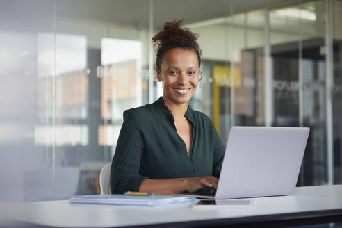 Porträt einer lächelnden Geschäftsfrau, die an einem Laptop am Schreibtisch arbeitet - RBF07777