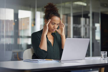 Portrait of pensive businesswoman at desk looking at laptop - RBF07779