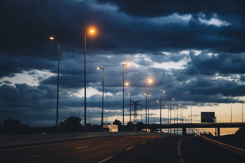 Spanien, Provinz Barcelona, Barcelona, Dunkle Gewitterwolken über der Stadtautobahn in der Abenddämmerung - OCMF01361