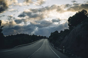 Spanien, Provinz Guadalajara, Wolken über leerer Landstraße in der Abenddämmerung - OCMF01362